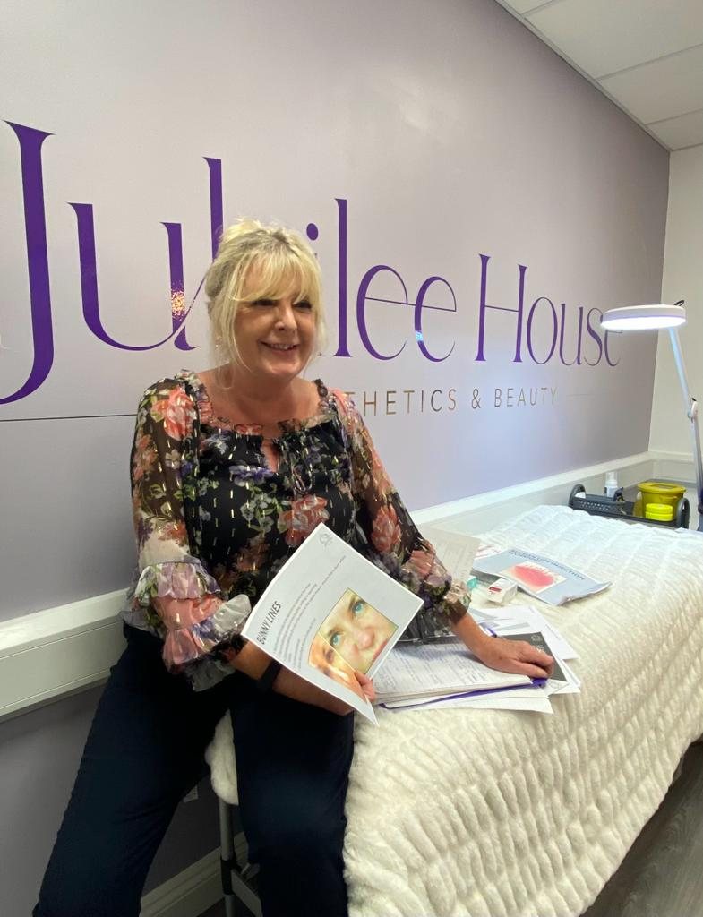 Mandy Drake seated in the treatment room beneath the Jubilee House Aesthetics & Beauty sign